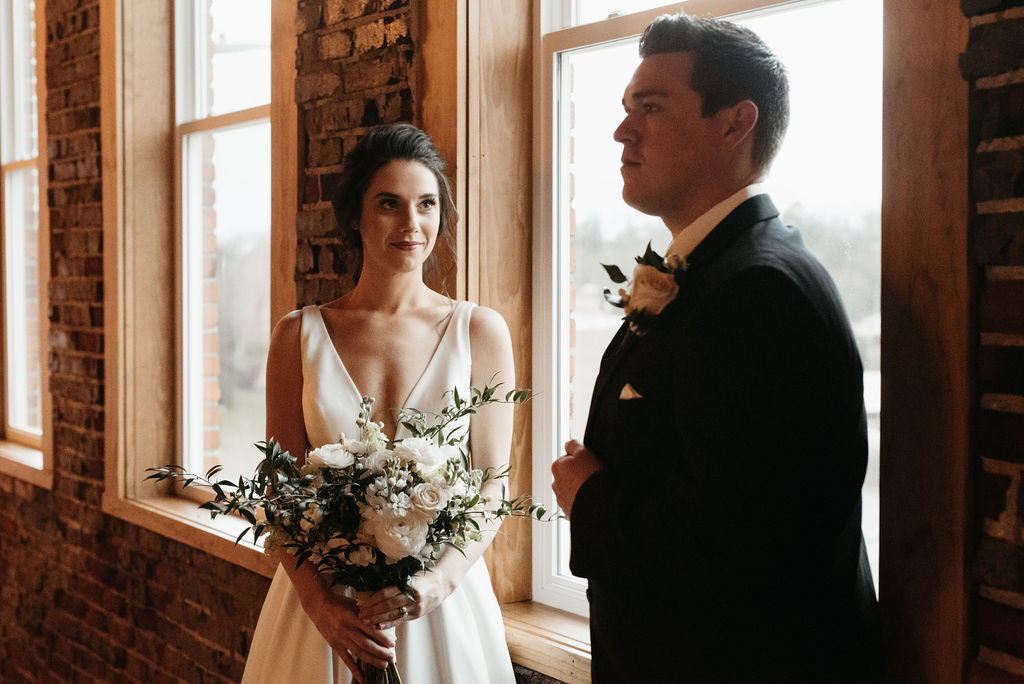 Bride and groom in front of windows with floral bouquet