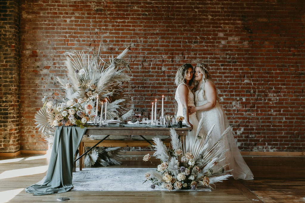 Brides posing at sweetheart table for boho wedding at White Star Station in Tennessee