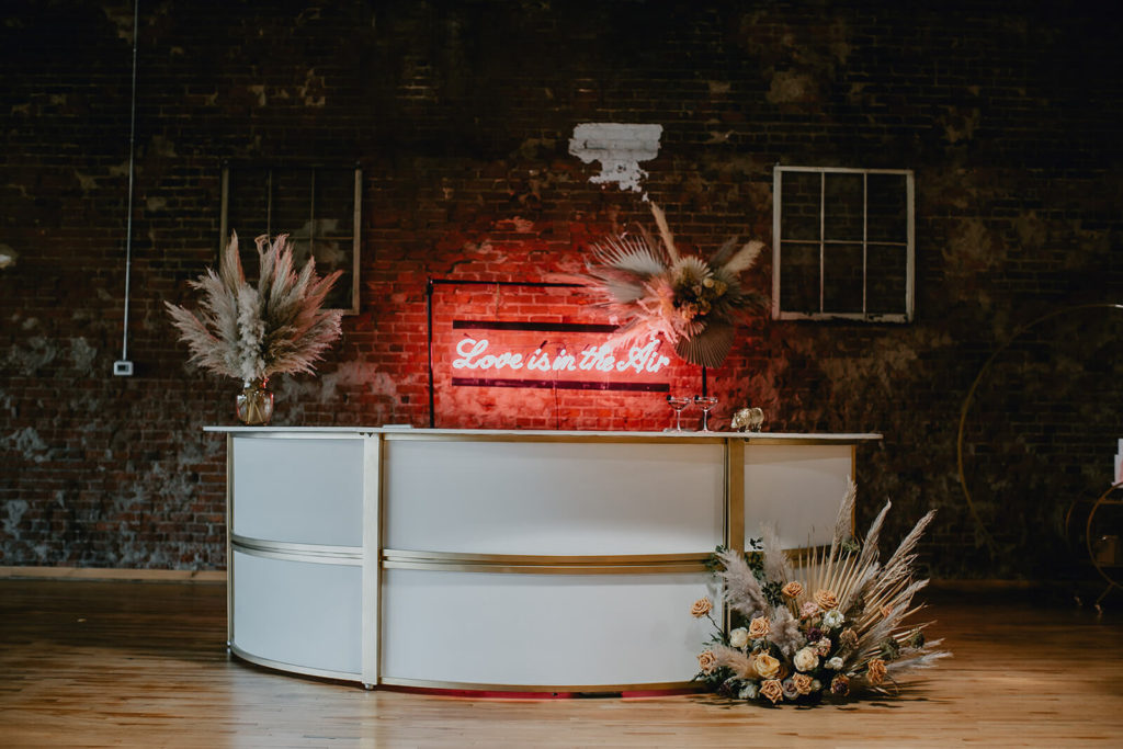 Custom round bar with gold detail, boho florals, and neon sign backdrop for intimate elopement